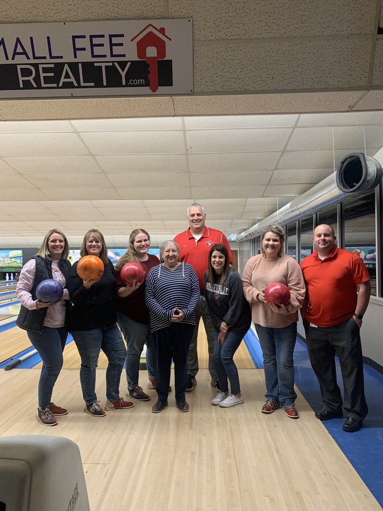 Staff posing in a bowling alley with bowling balls